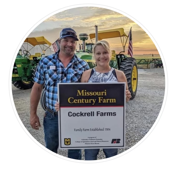 man and woman on a farm in front of tractors smiling and holding "Missouri Century Farm" plaque